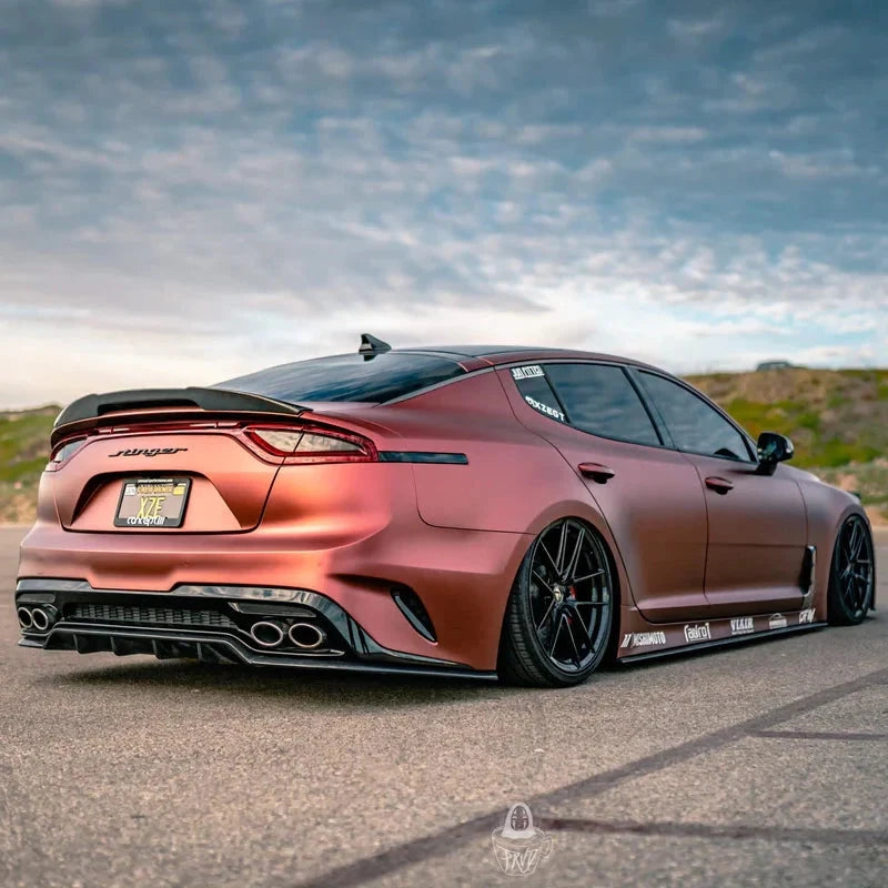 ADRO front lip on Kia Stinger CK, front three-quarter view, matte copper finish, parked under cloudy sky.