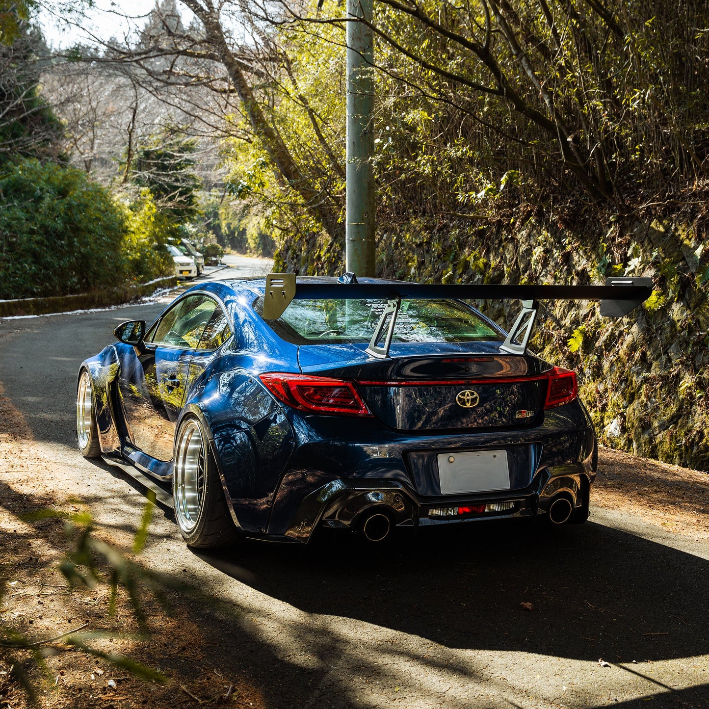 Dark blue widebody rear with large wing, flared fenders, rear diffuser, dual exhaust