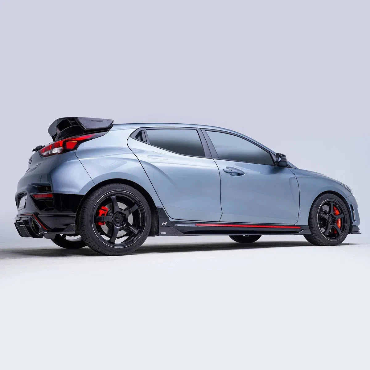 ADRO carbon fiber rear diffuser on Hyundai Veloster N, side view showing black wheels and red calipers.