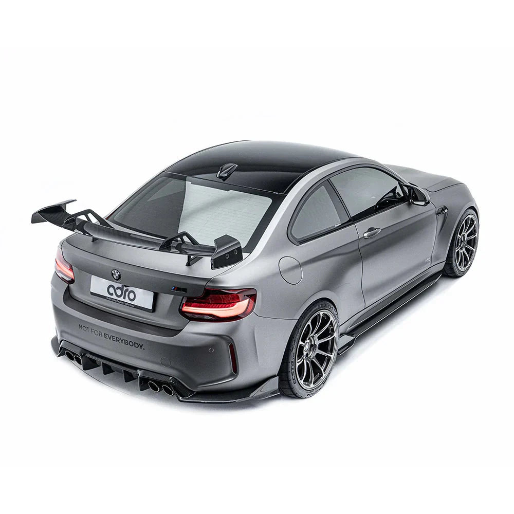 ADRO carbon fiber side skirts on BMW G8X M4, installed view from rear left, matte gray car on white background.