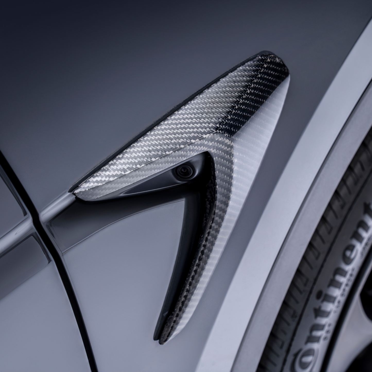 ADRO carbon fiber side camera for Tesla Model Y, detail view near Continental tire showing aero features.