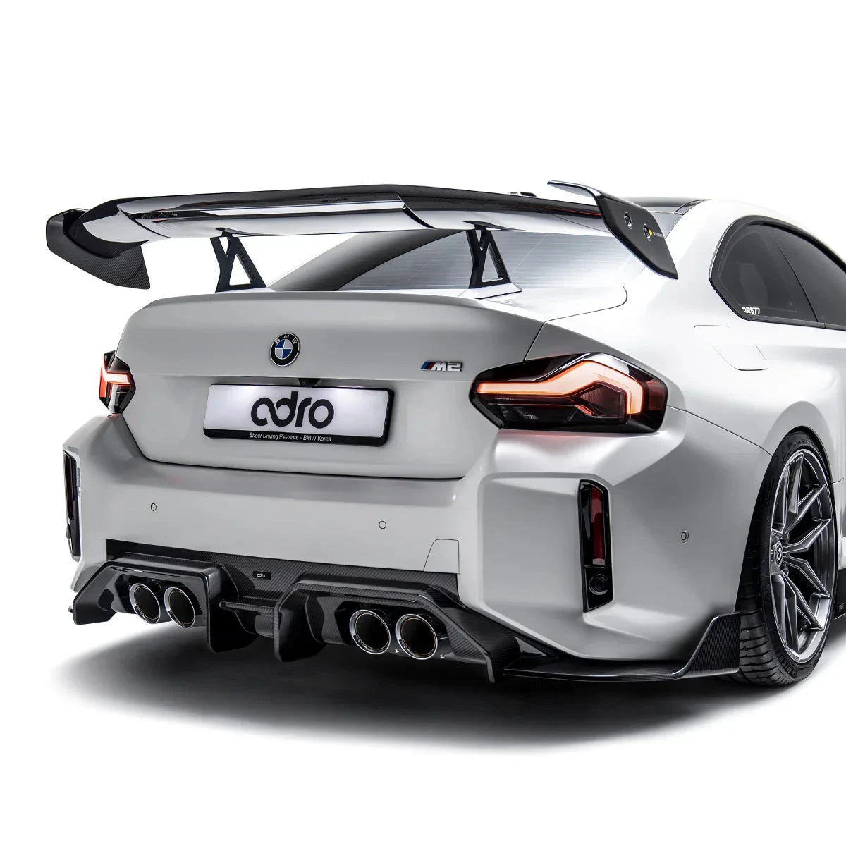 ADRO rear diffuser for BMW G87 M2, rear view of white car with quad exhausts on white background.