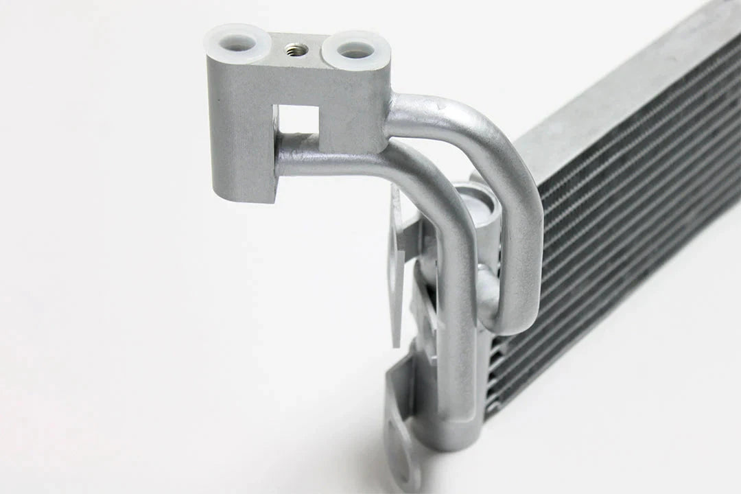 Silver oil cooler close-up with U-shaped pipes and top threaded fittings
