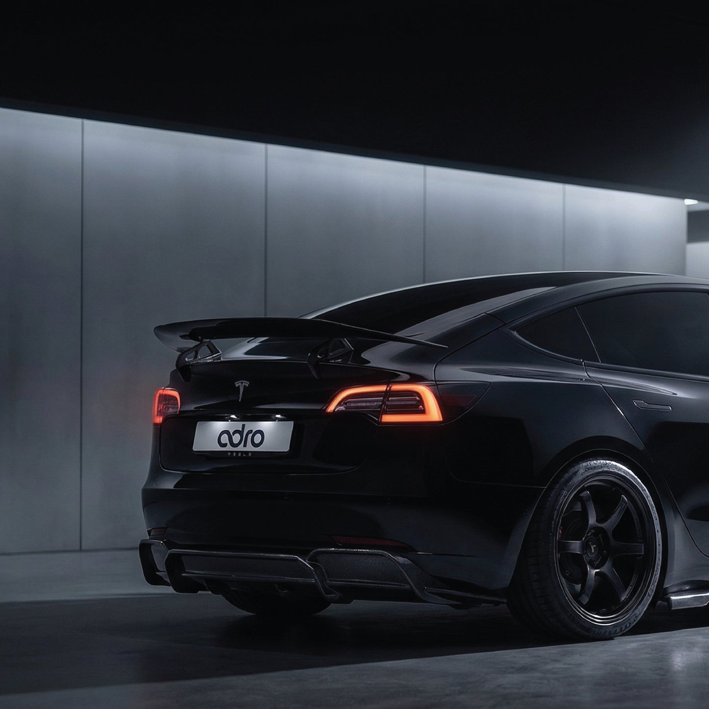 ADRO US AT-S Swan Neck Wing on Tesla Model 3, rear three-quarter view, parked indoors with taillights illuminated.