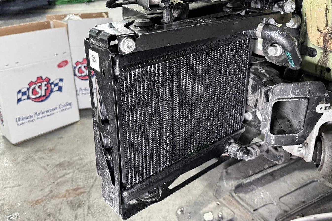 Auxiliary radiator installed in vehicle bay, black mesh core with visible hoses.
