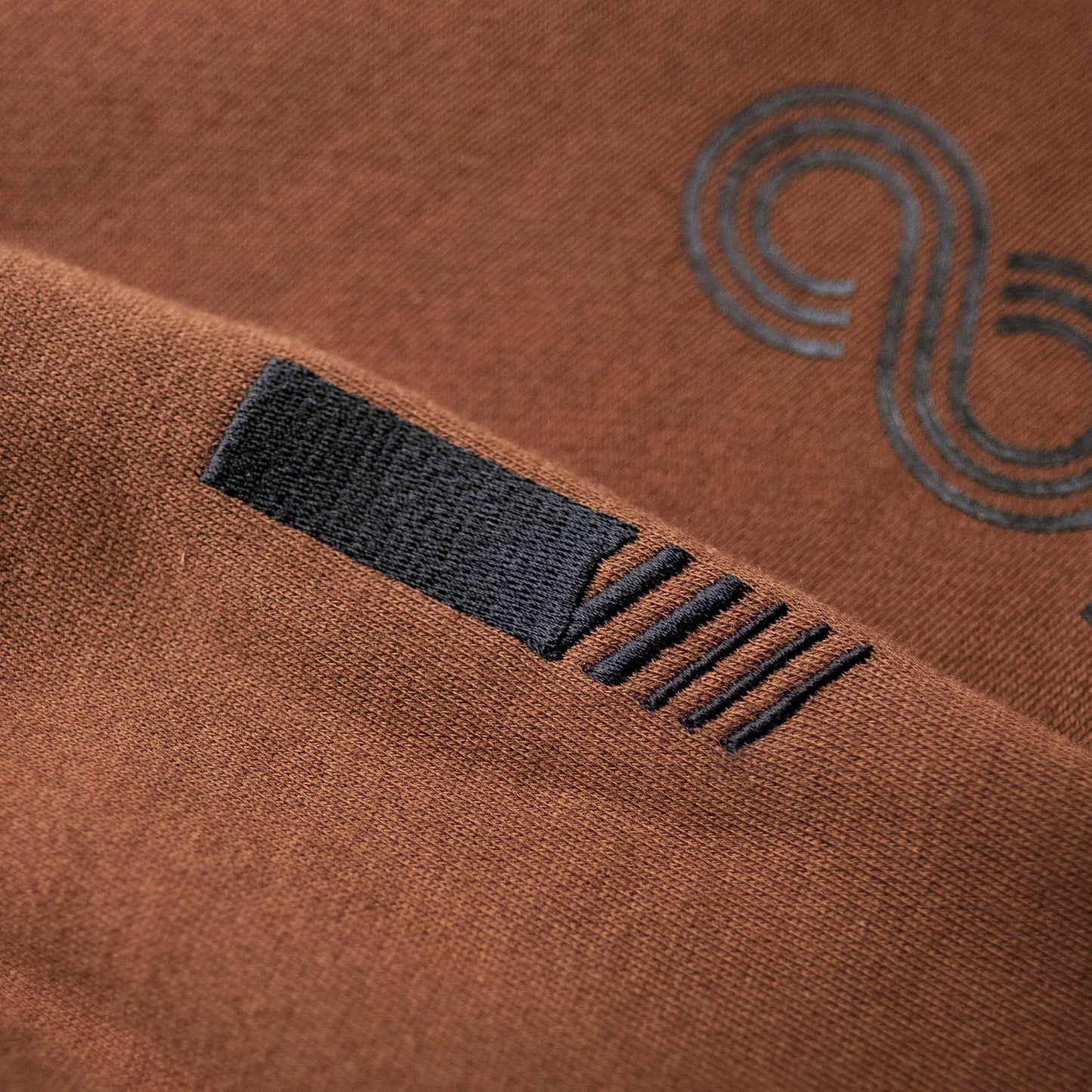 Brown hoodie sleeve seam with black logo and inner label