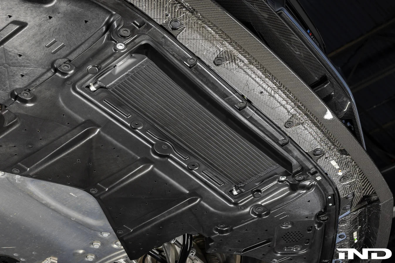 Installed engine oil cooler with black finned core under engine bay cover
