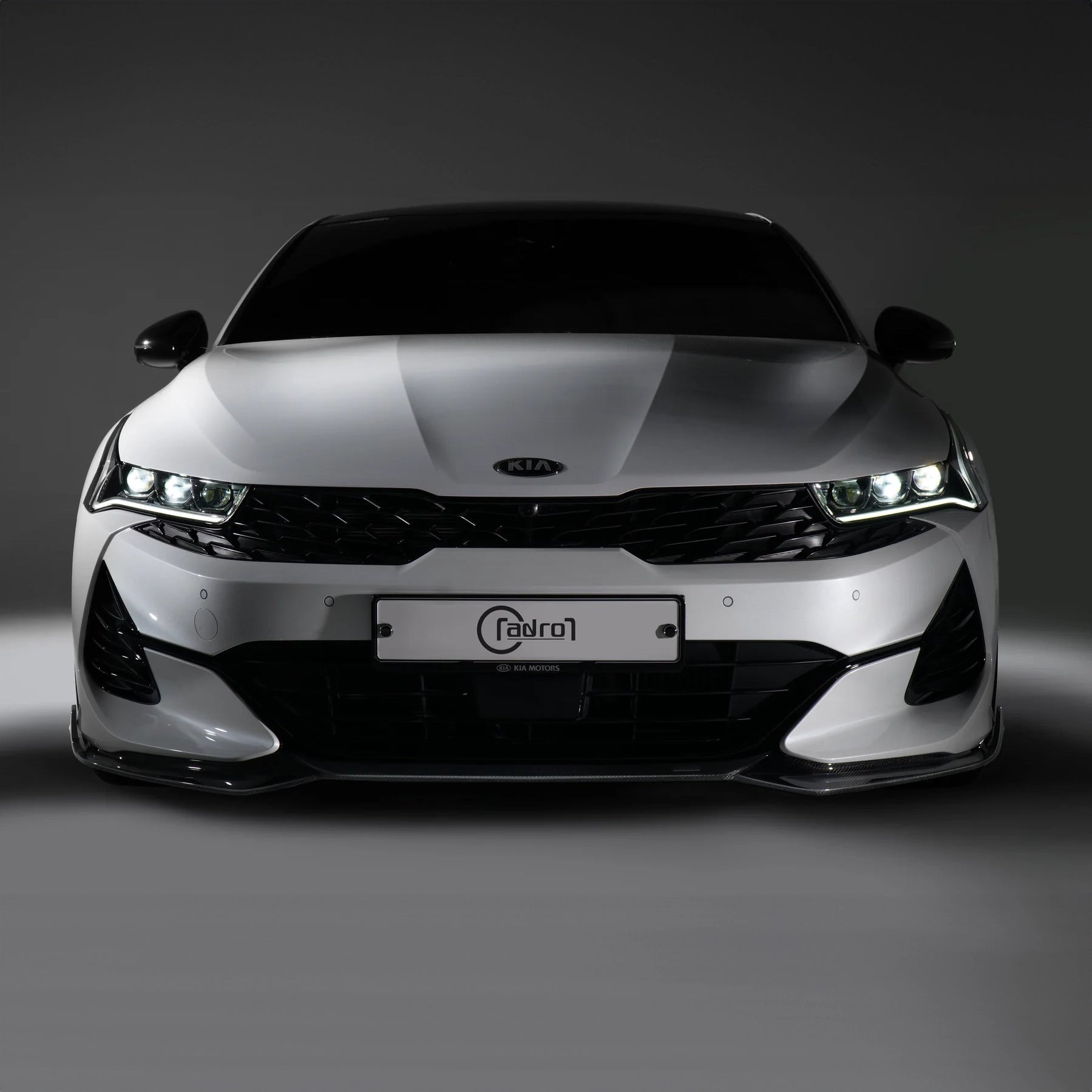 White sport sedan front view with KIA badge and illuminated headlights