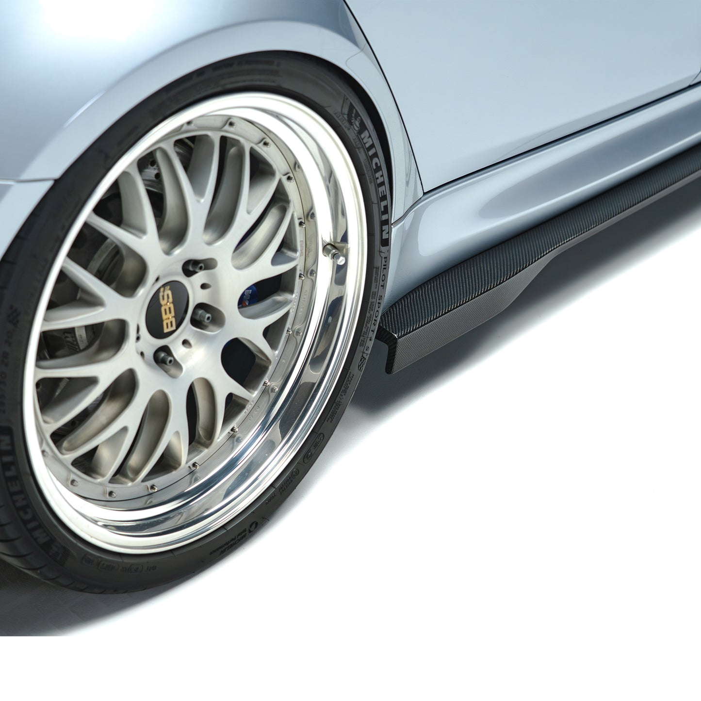Carbon fiber side skirt close-up with dark weave texture by front wheel.