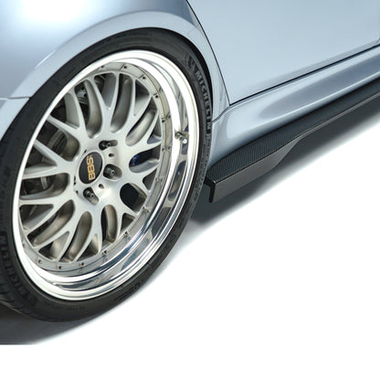 Carbon fiber side skirt close-up with dark weave texture by front wheel.