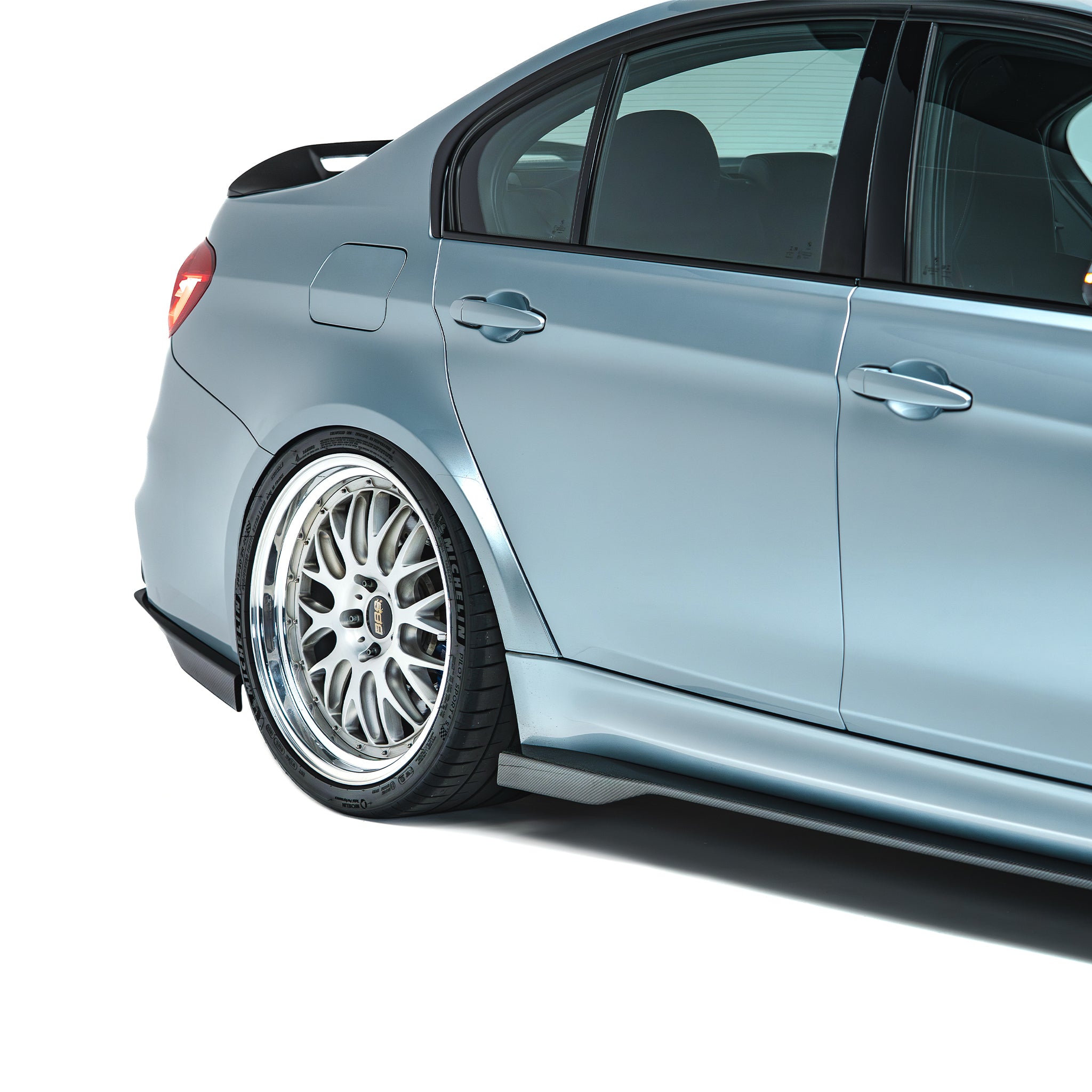 Carbon fiber side skirts, dark rocker-panel trim on light blue sedan side.