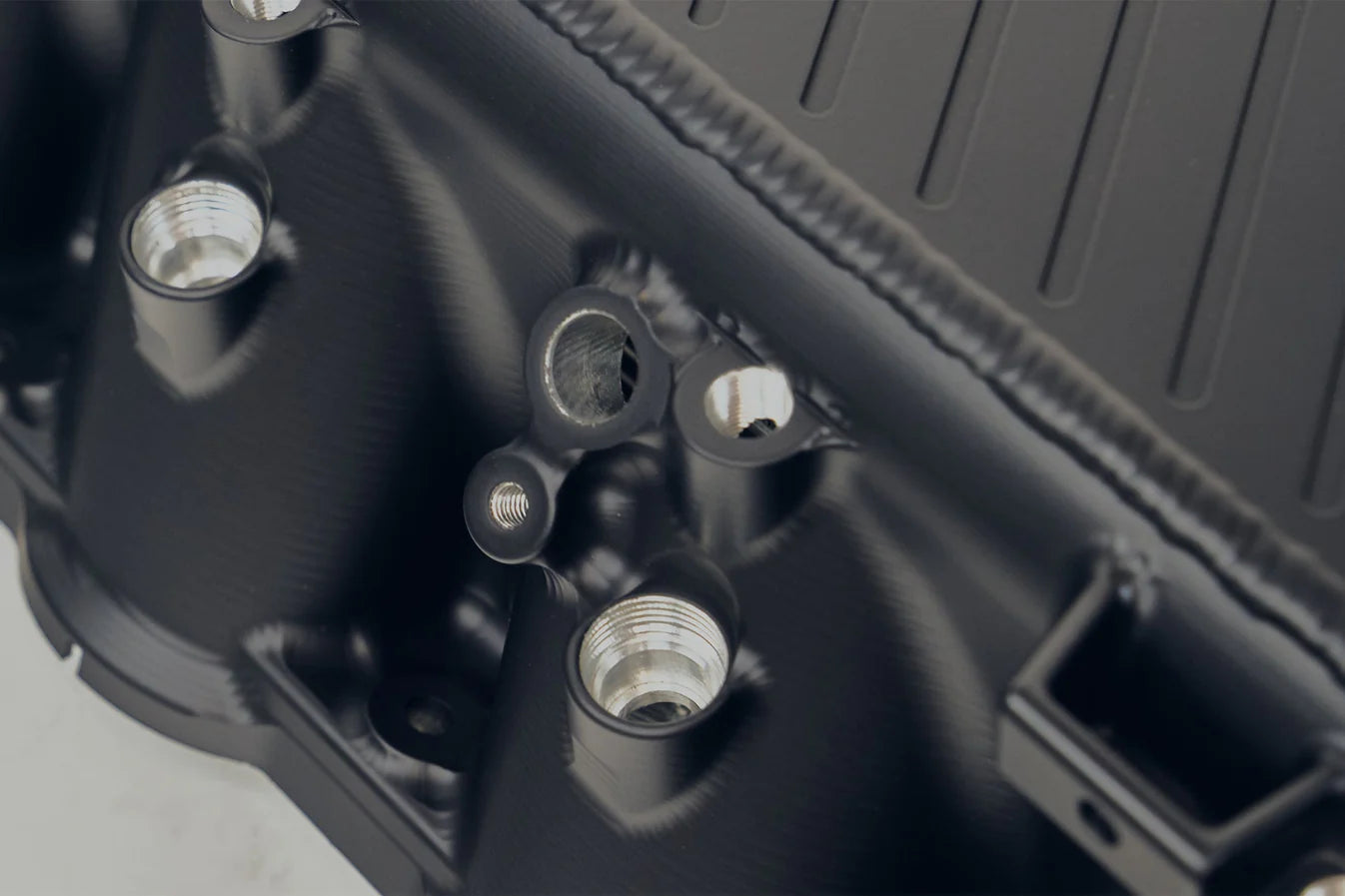 Charge-air cooler manifold, black close-up with threaded ports and embossed panel details
