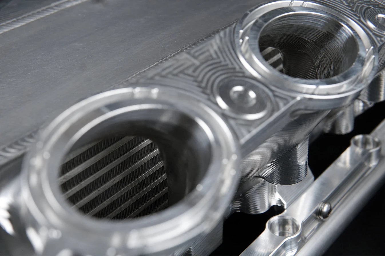 Charge-air cooler manifold, silver end close-up with circular inlet/outlet ports and grille