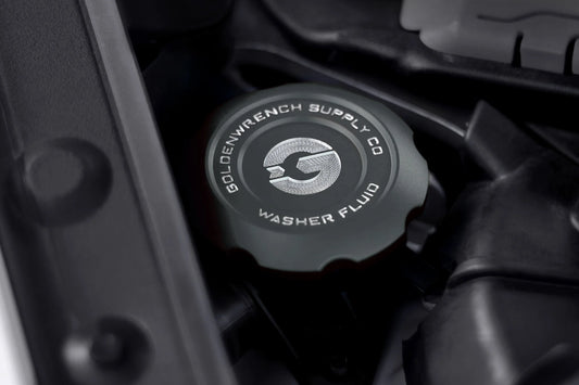 Washer fluid cap in dark gray with "WASHER FLUID" logo, shown in engine bay